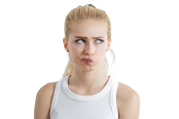 Blonde woman with pursed lips and crossed eyes, wearing a white tank top, against a white background.